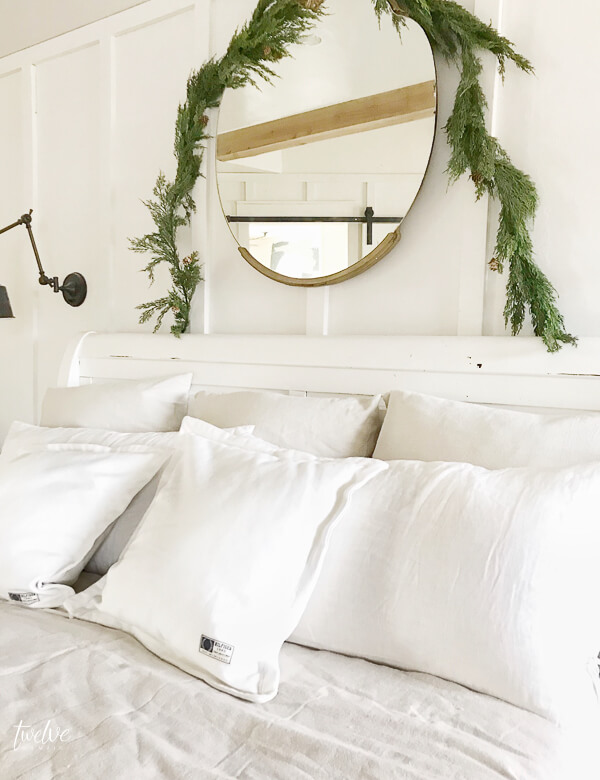 Simple and elegant Scandinavian farmhouse style Christmas bedroom decor. White linens, antique gold mirror, faux cedar garland, and tons of white pillows!
