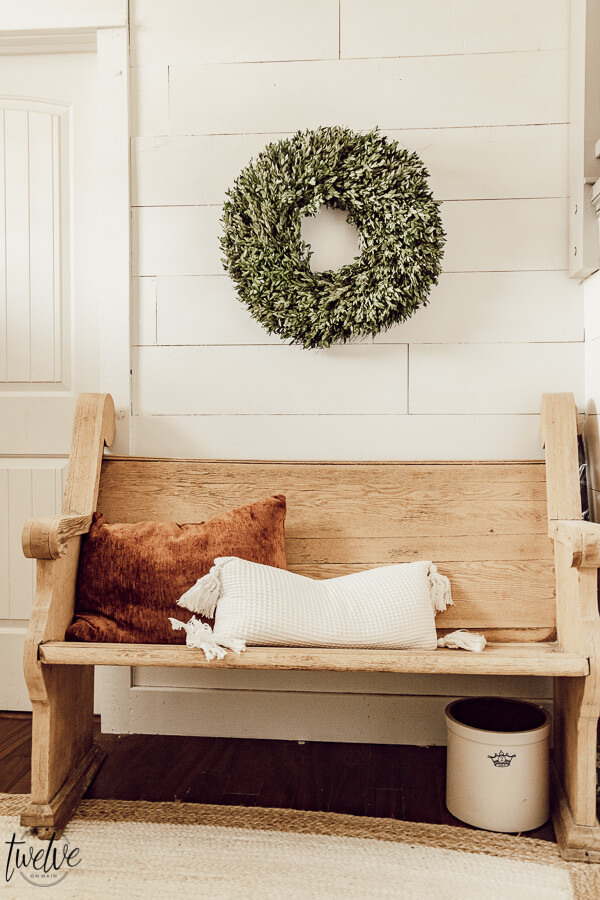 Simple winter decor in the entryway using a festive boxwood wreath and a warm rust colored pillow.