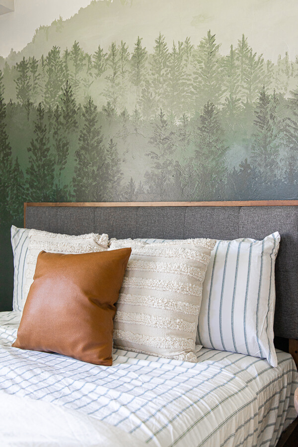 Gorgeous guest bedroom complete with a cozy bed, beautifully painted custom forest wall mural, cozy seating, and so much more.