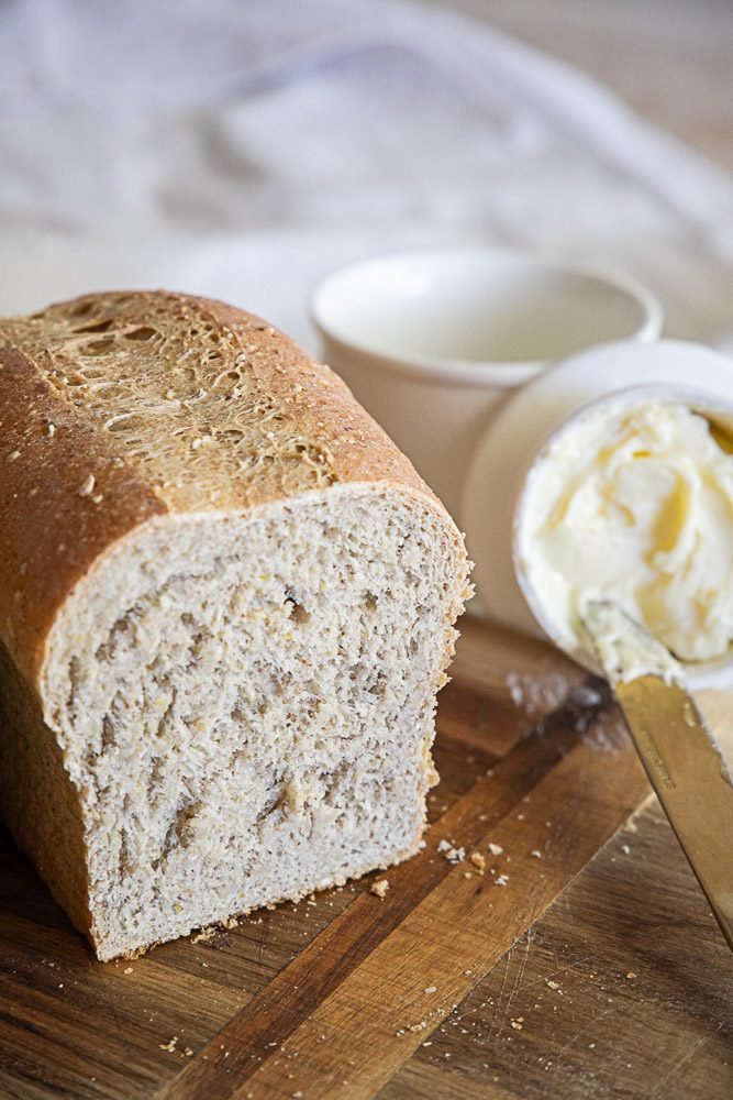Multigrain sandwich bread sitting on a cutting board with a spread of softened butter